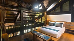 Ein Zimmer mit hohen Decken, einem großen Bett, Holzboden und Blick durch ein mit Vorhängen drapiertes Fenster.