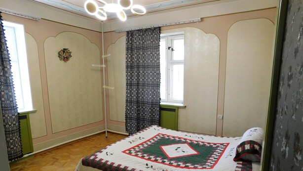 Un dormitorio con cama, ventana con cortinas, lámpara de pared y una puerta.