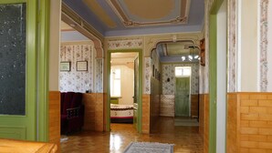 Un pasillo con suelo de madera, paredes verdes y papel tapiz floral. Se ve una cama y una puerta verde al fondo.