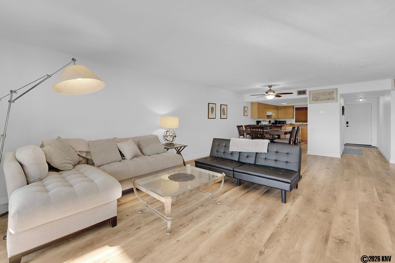 A modern living room with a sofa, a coffee table, and a dining area in the background.