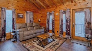 Ein gemütliches Blockhaus-Interieur mit Ledersofa, Holztisch und gemusterten Vorhängen.