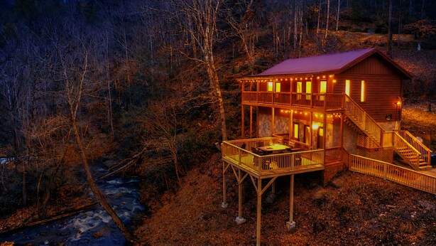Eine Holzhütte mit Balkon und Treppe, umgeben von Bäumen und einem Fluss.