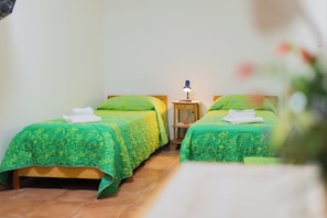 Een kamer met twee bedden, elk voorzien van groen beddengoed en een houten hoofdbord. Daartussen staat een nachtkastje met een lamp.