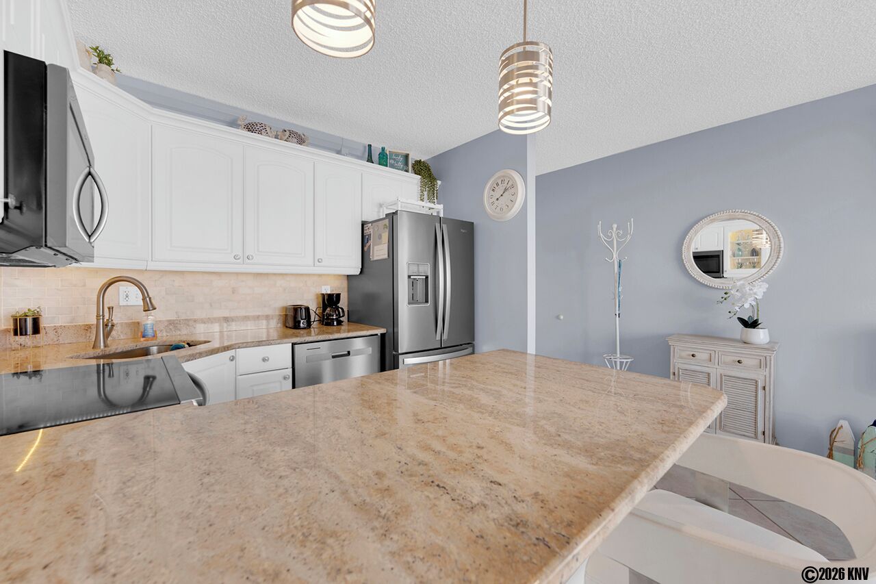 A modern kitchen with white cabinets, a granite countertop, stainless steel appliances, and pendant lighting.