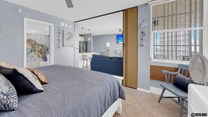 Een moderne slaapkamer met een groot bed, een bureau, een stoel en een raam met jaloezieën.