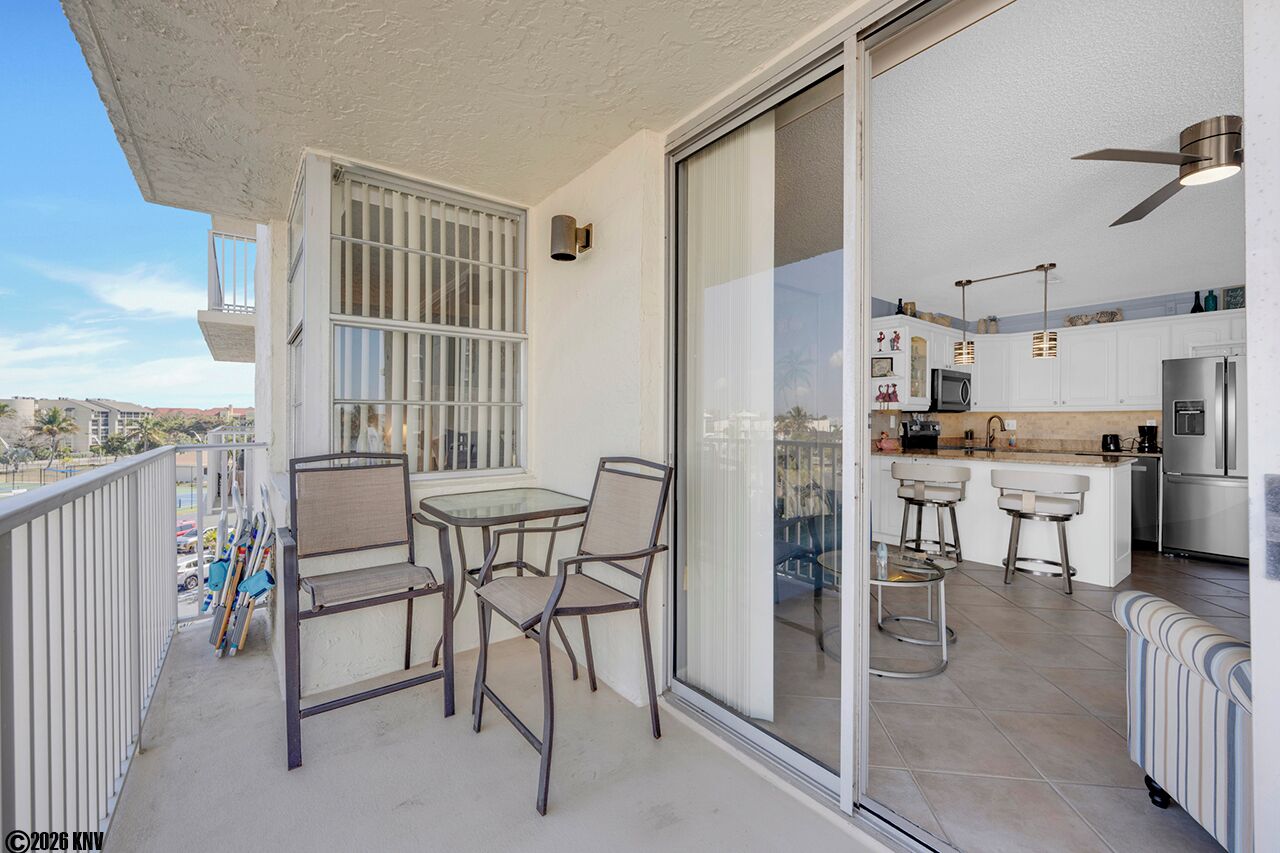 A balcony with a glass door leading to a kitchen area, featuring a bar stool, a dining table, and a sofa.