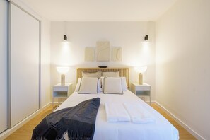 Habitación de hotel ordenada con una cama grande, lámparas de noche y una obra de arte colgada en la pared.