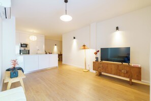 Una sala de estar moderna con un televisor de pantalla plana, un mueble de madera y una cocina al fondo.