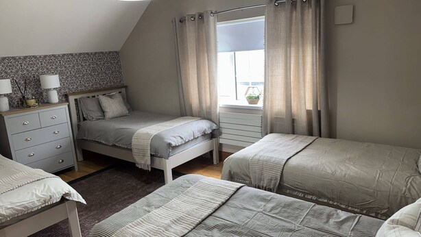 Ein Schlafzimmer mit zwei Betten, einem Schminktisch, einem Fenster mit Vorhängen und einer Wand mit Muster.
