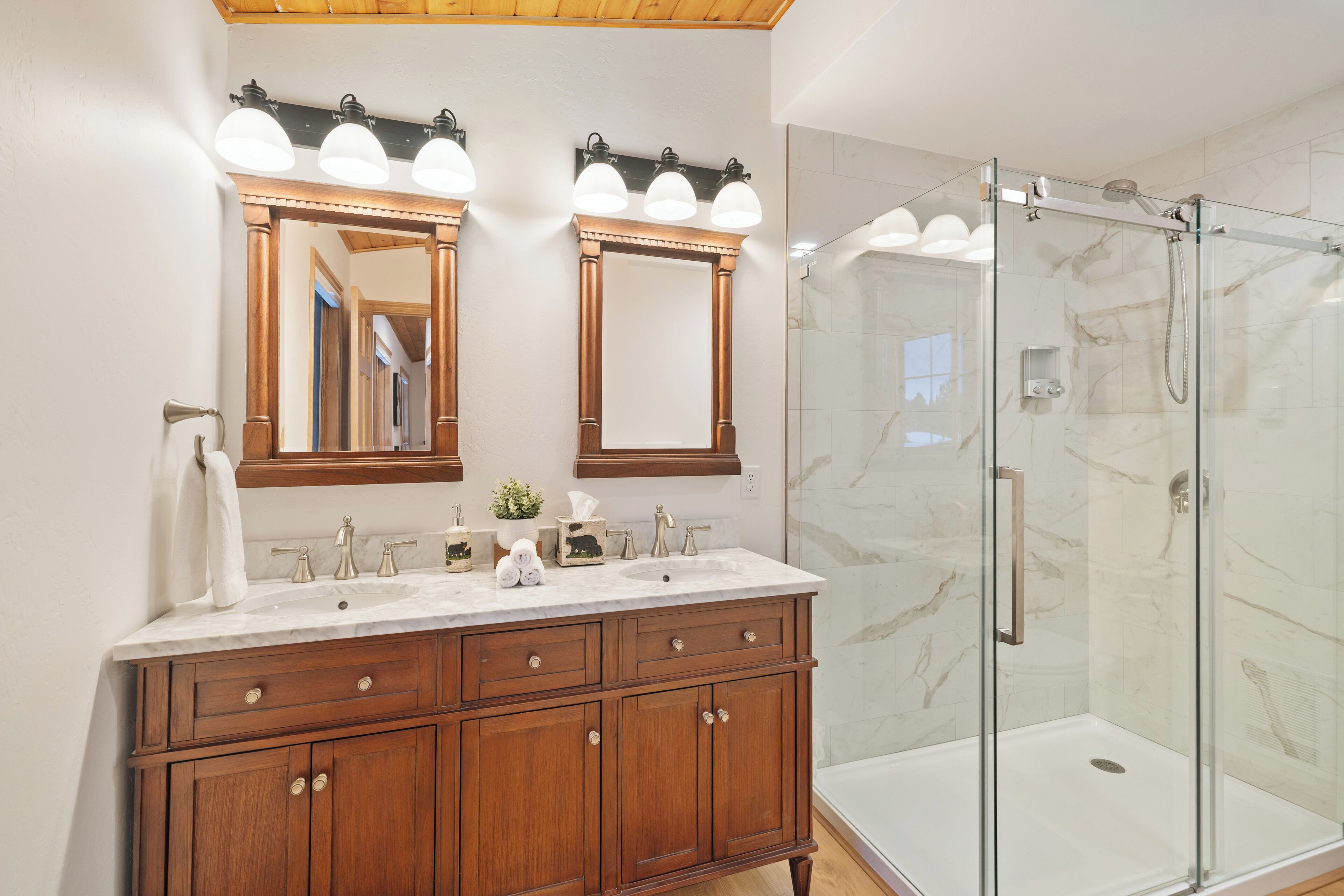 Une salle de bain avec un meuble-lavabo en bois, deux miroirs, une cabine de douche en verre et des murs en marbre.