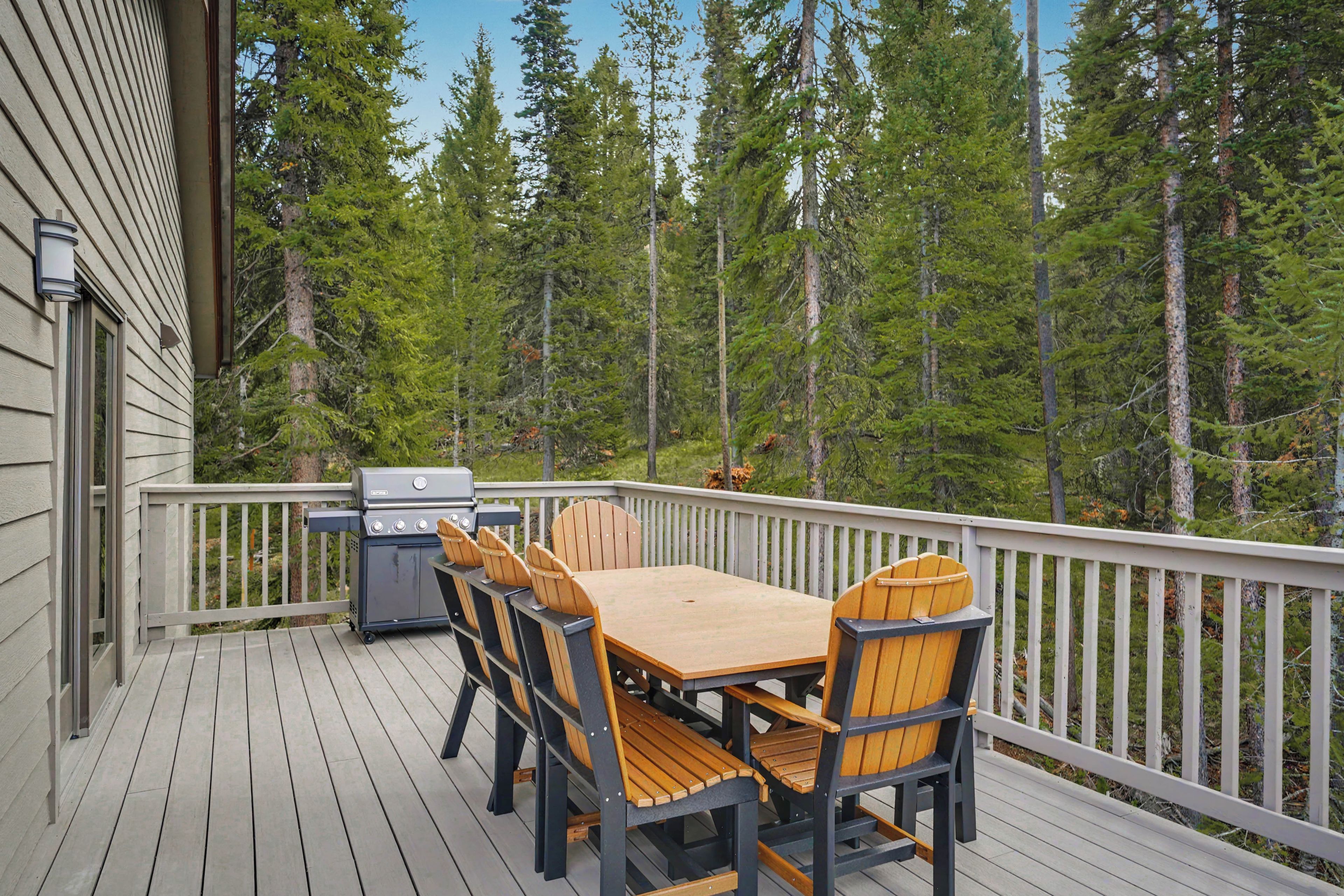 A deck with a table and chairs, a grill, and a view of a forest.