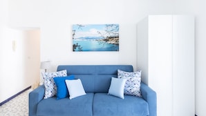 A blue sofa with patterned cushions, a framed landscape painting, and a lamp on a white floor with blue floral tiles. - SEA FRONT TERRACE APARTMENT MARINA GRANDE SORRENTO (Sorrento)