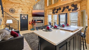 A wooden cabin interior with a fireplace, a dining area, and a staircase. - New Cabin Rental-Bowling Alley-Hot Tub-Adjustable Beds-Luxury Cabin Rentals (Sevierville)