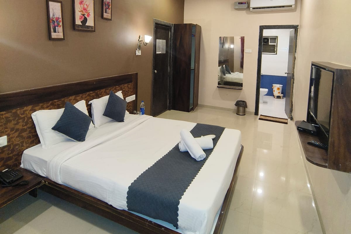 A hotel room with a large bed, a ceiling fan, an air conditioning unit, a television, and a bathroom visible through an open door.