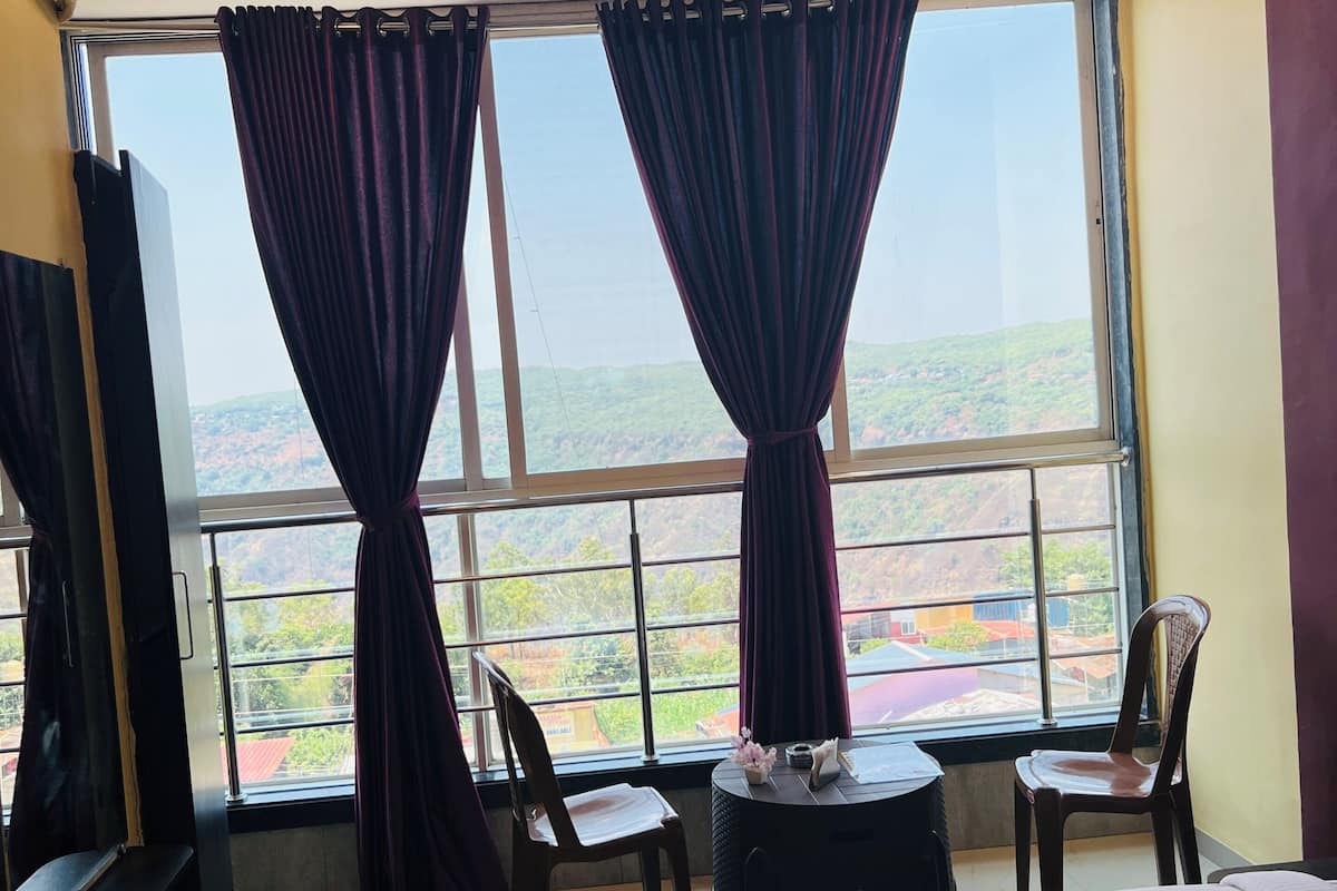 A hotel room with a bed, a small table, two chairs, a TV, and a large window with curtains.