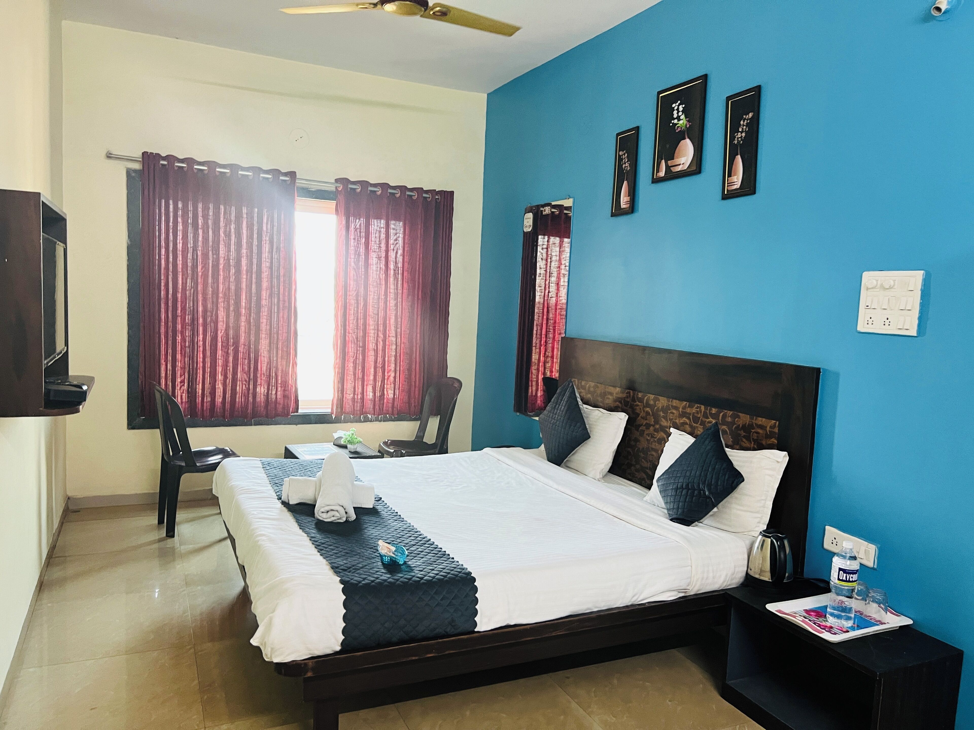 A hotel room with a bed, a desk, a chair, a ceiling fan, and a window with curtains.