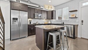 Una cocina moderna con electrodomésticos de acero inoxidable, una isla con encimera de granito y un taburete de bar.