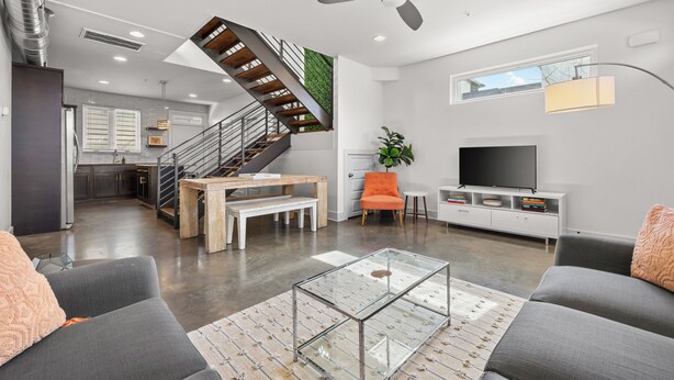 Una sala de estar moderna con una escalera, un televisor de pantalla plana y un comedor.