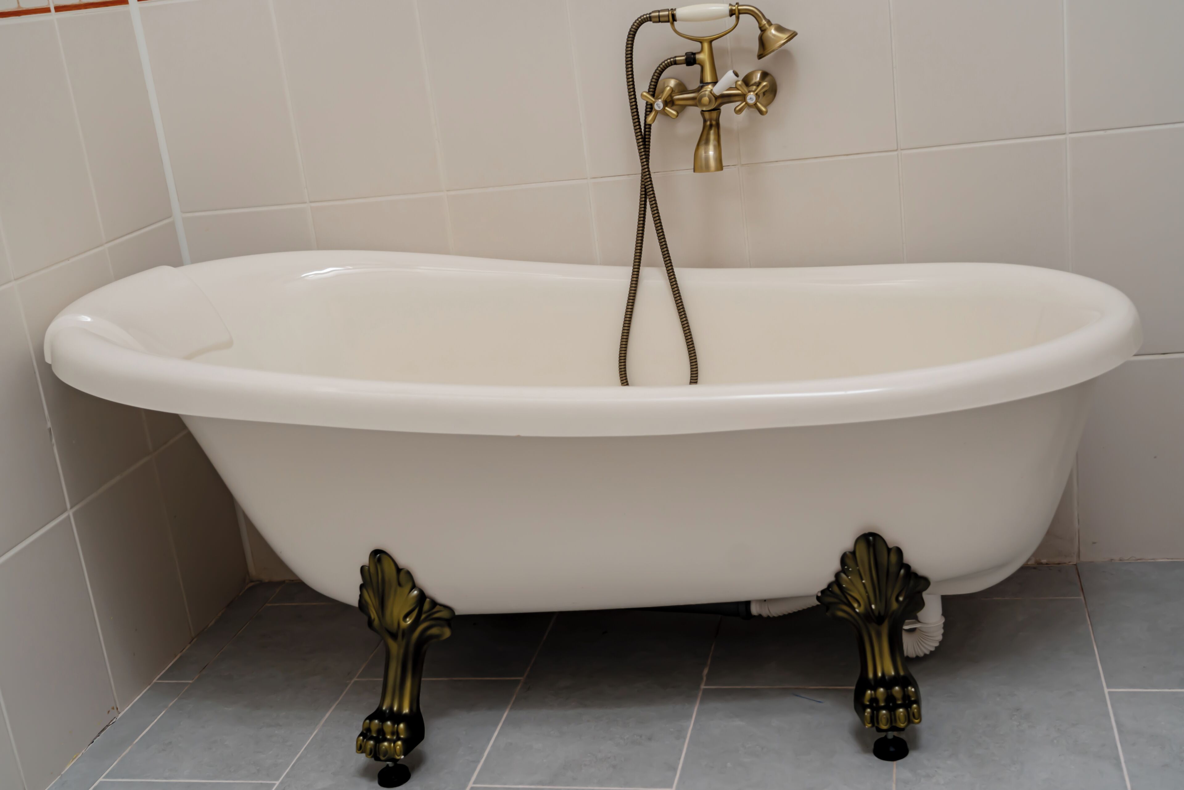 A white freestanding bathtub with brass fixtures and ornate legs.