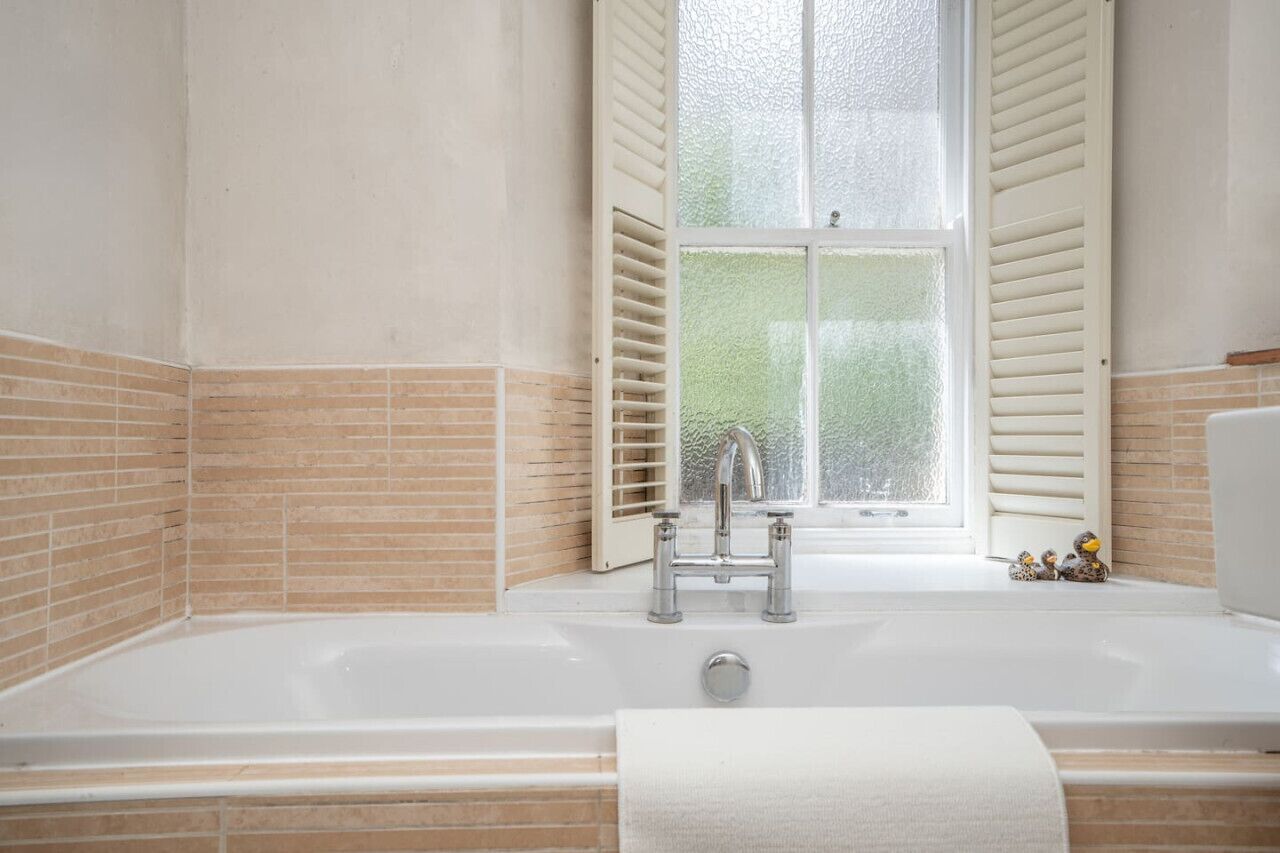 Une salle de bain avec une baignoire, une fenêtre avec des volets et un porte-serviettes.