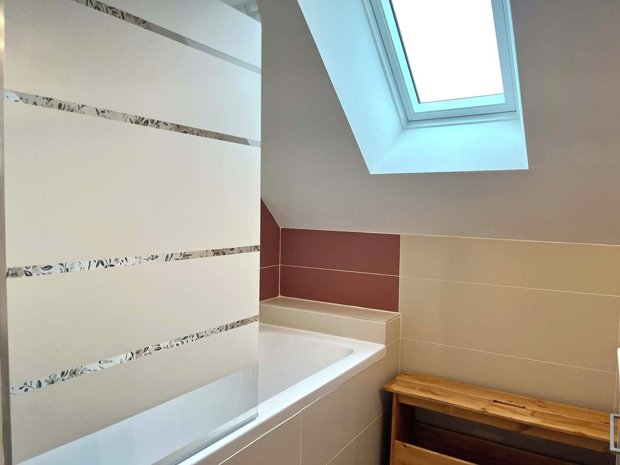 Une salle de bain avec un puits de lumière, une baignoire et un banc en bois.