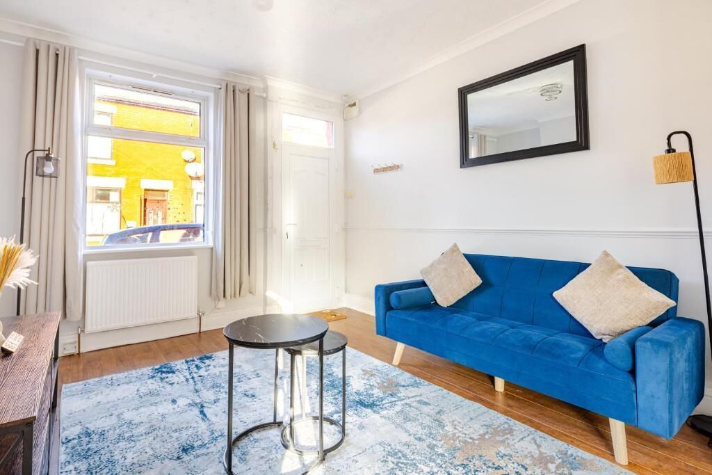 A living room with a blue sofa, a round coffee table, and a large window with curtains.