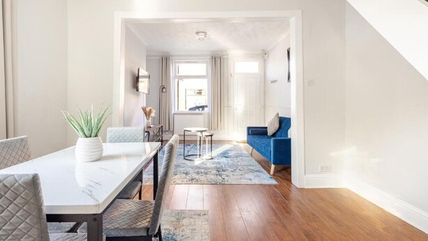 Ein modernes Wohnzimmer mit einem weißen Esstisch, einem blauen Sofa und einer Treppe.