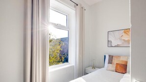 Ein Schlafzimmer mit einem großen Bett, einem Nachttisch, einem gerahmten Bild und einem Fenster mit Vorhängen.