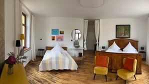 Une chambre d’hôtel comprenant un lit, deux chaises, une table de chevet, un miroir et des œuvres d’art accrochées aux murs.