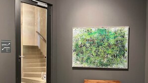Un escalier menant à l’étage supérieur, un banc en bois et un grand tableau abstrait accroché au mur.