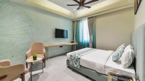 A modern hotel room with a bed, a desk, a chair, a TV, and a ceiling fan. - Bhagwati Luxuria Hotel  (Indore)