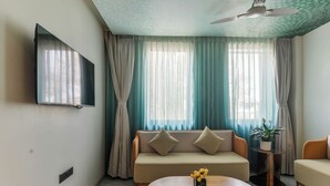 A modern living room with a sofa, a coffee table, a TV mounted on the wall, and a ceiling fan. - Bhagwati Luxuria Hotel  (Indore)