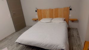 Un dormitorio con cabecera de madera, dos mesitas de noche, colcha a rayas y suelo de baldosas grises.