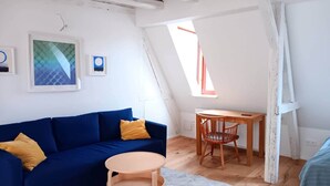Quarto loft acolhedor com teto inclinado, sofá azul, escrivaninha de madeira e uma pequena mesa redonda.