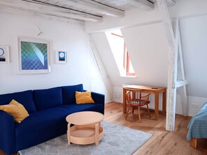 Ein gemütliches Schlafzimmer im Loft-Stil mit schrägen Wänden, einem blauen Sofa, einem Holztisch und einem kleinen runden Tisch.
