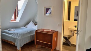 Um quarto com uma cama, uma pequena mesa de cabeceira de madeira, um quadro emoldurado e uma porta que dá para um banheiro.