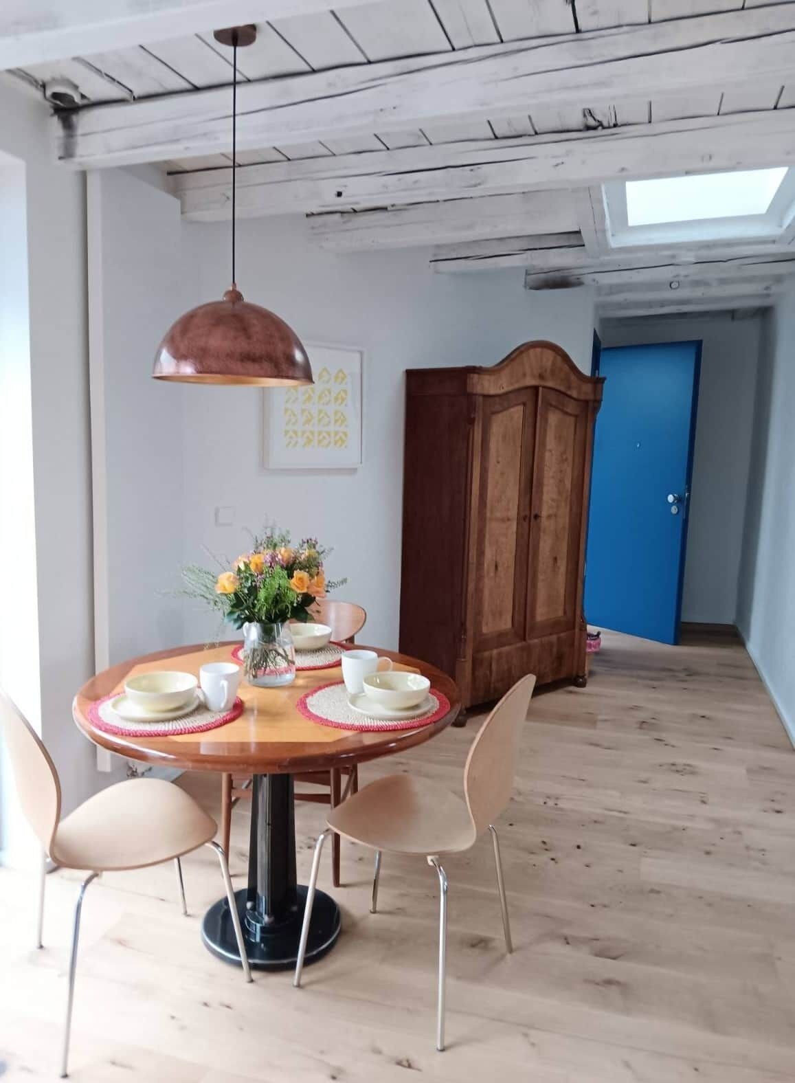 Un coin repas comprenant une table ronde en bois, quatre chaises, un vase avec des fleurs et une suspension.