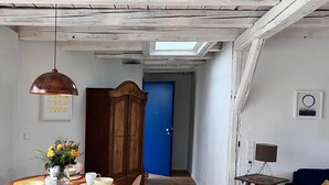 Uma sala de jantar com uma mesa de madeira, cadeiras e uma luminária pendente. Uma porta azul é visível ao fundo.