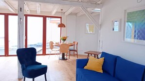 Um quarto espaçoso com um sofá azul, uma poltrona azul e uma mesa de jantar com cadeiras.