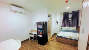 Hotellihuone, jossa on sänky, työpöytä, jääkaappi ja ilmastointilaite.