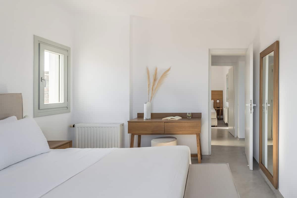 A bedroom with a bed, a wooden desk, a radiator, and a window.