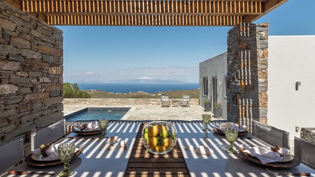 A dining area with a view of the sea, stone walls, and a pool. - NEVERMIND VACATIONS VILLAS (Kea)