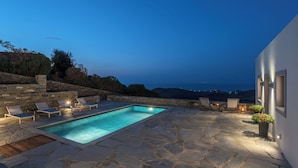 A stone pool with lounge chairs and a view of the sea at dusk. - NEVERMIND VACATIONS VILLAS (Kea)