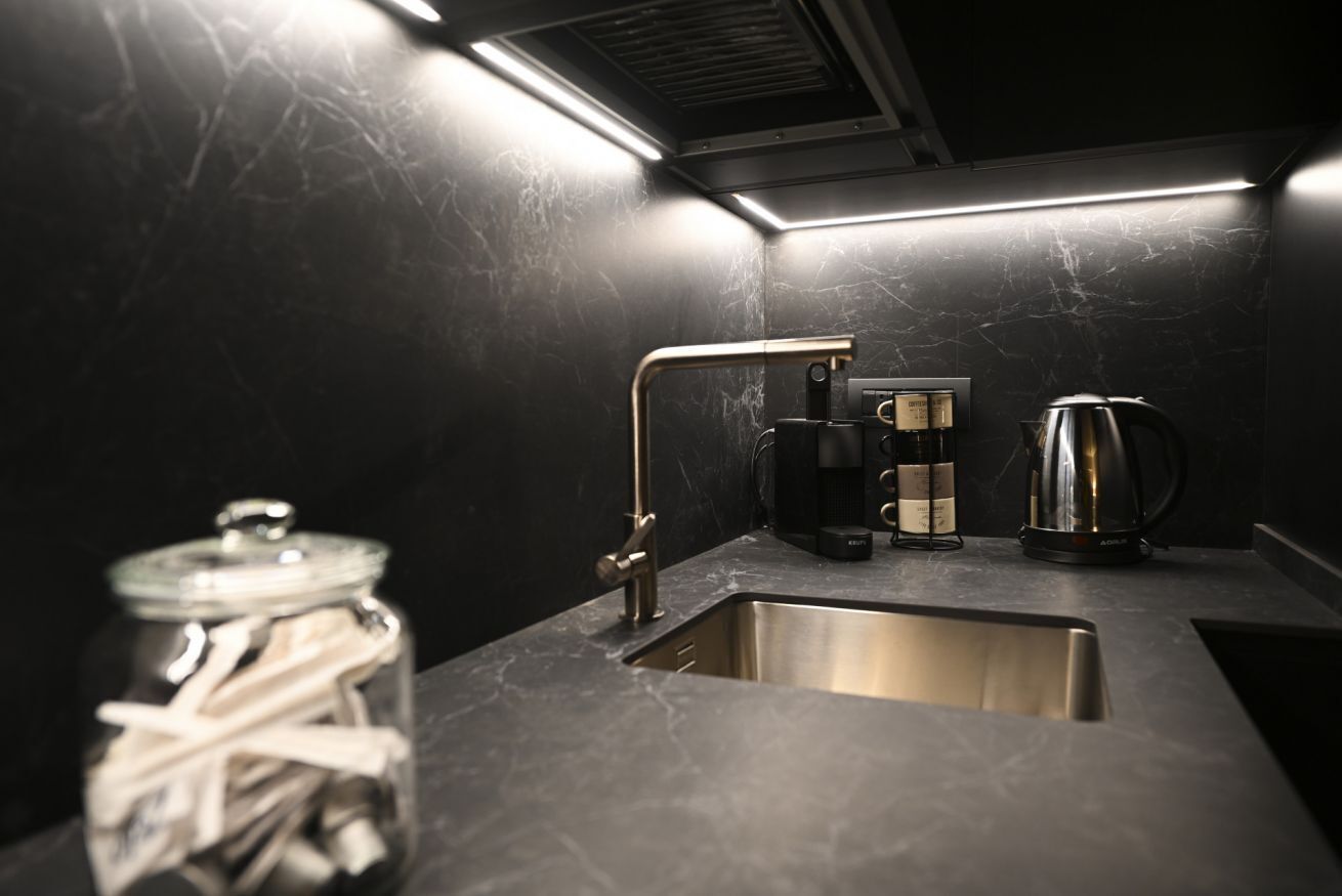 Une cuisine moderne dotée d’un évier en acier inoxydable, d’une machine à café et d’une bouilloire posées sur le plan de travail.