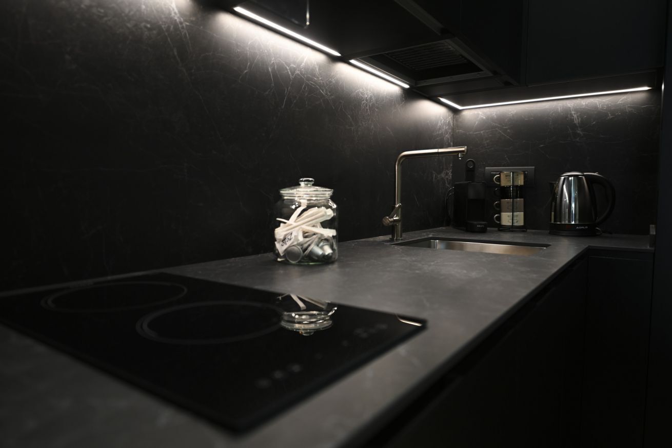 Een moderne keuken met een zwart aanrecht, een glazen pot met keukengerei, een koffiezetapparaat en een waterkoker.