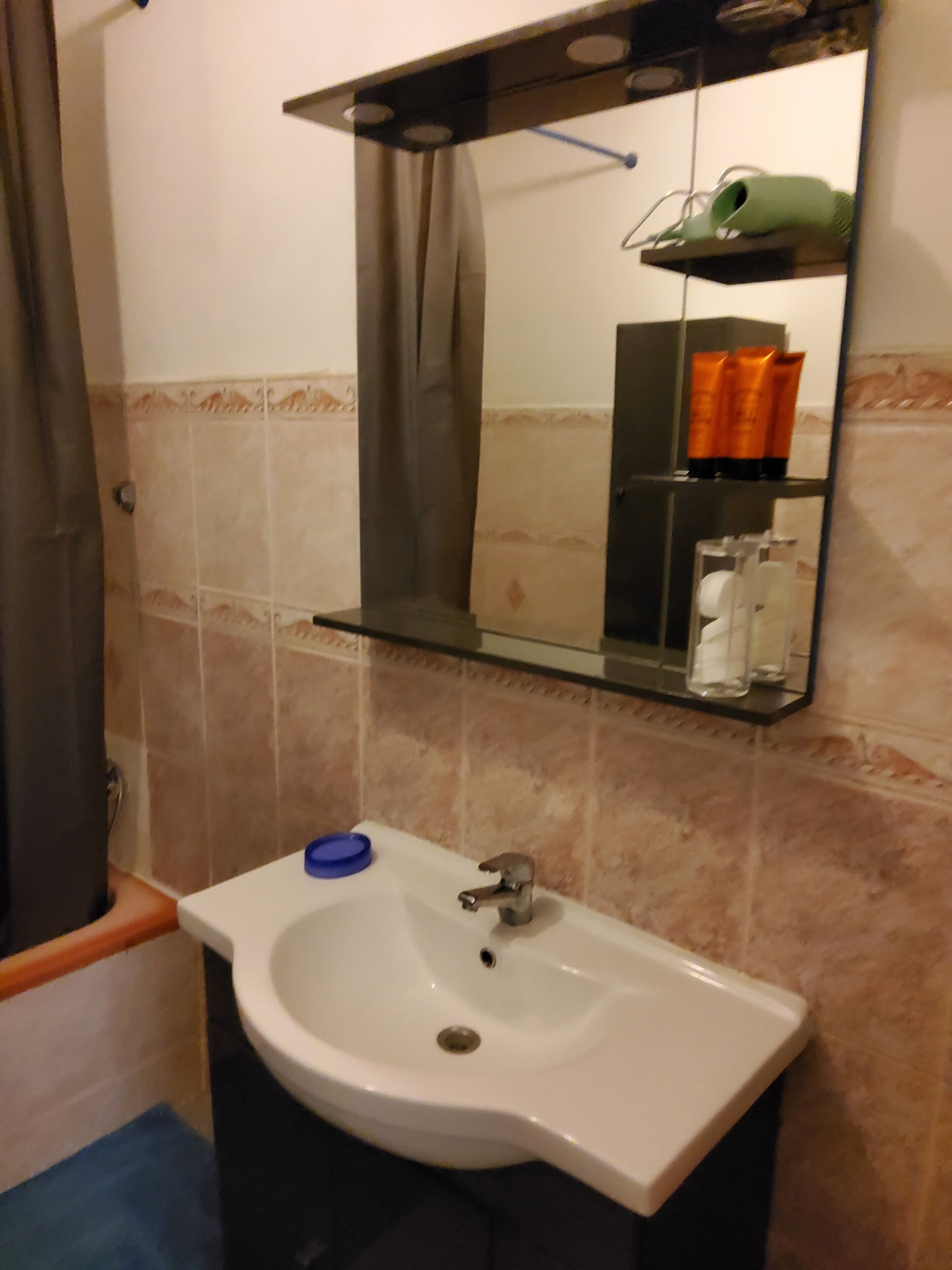 Une salle de bain avec un lavabo blanc, un miroir au-dessus et une étagère contenant des articles de toilette.