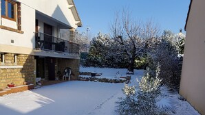Un patio cubierto de nieve con un edificio de piedra, un balcón y una pequeña zona ajardinada.