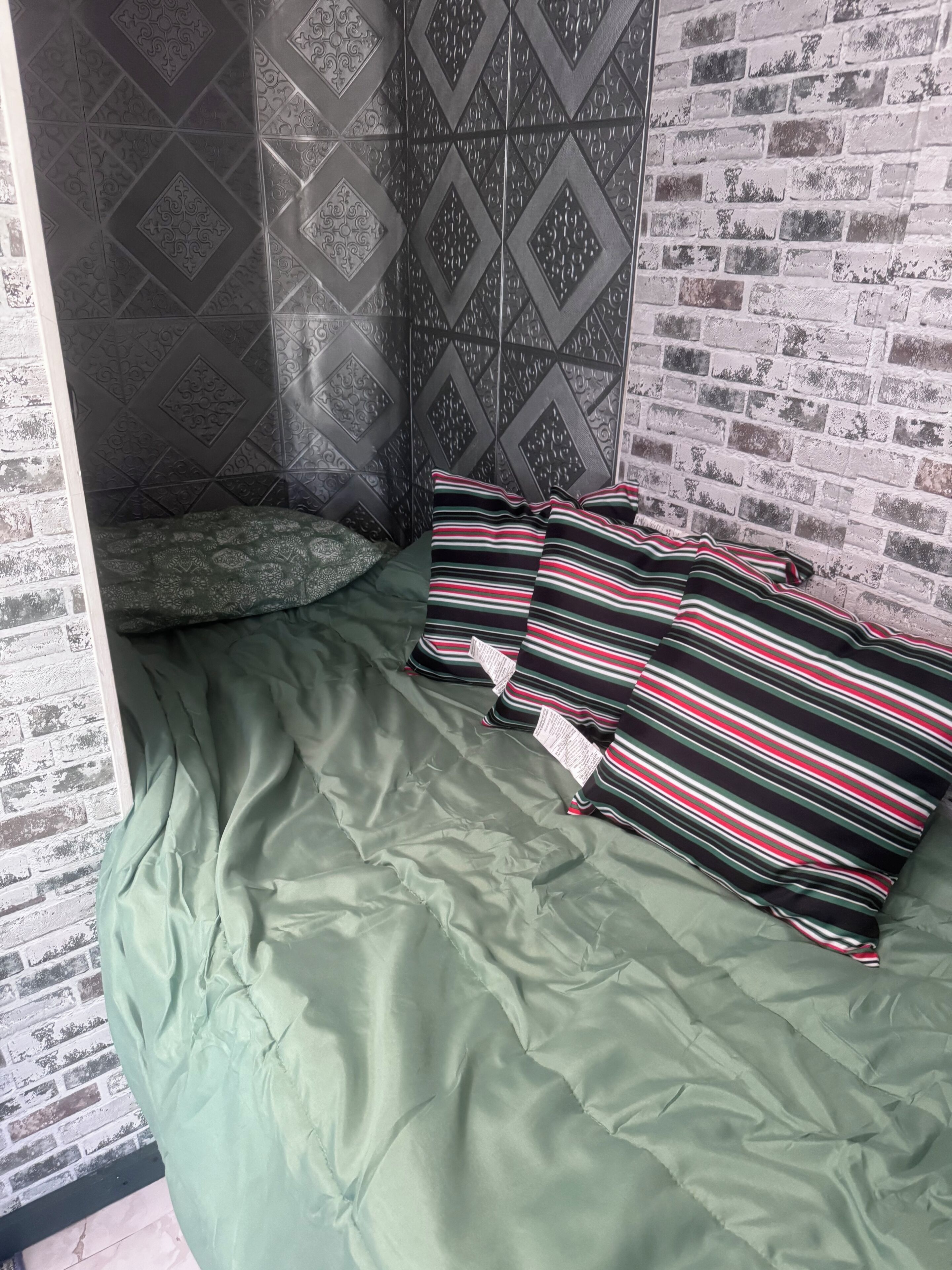 A room with a green bed, striped pillows, and a brick-patterned wall.