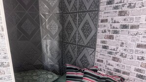 Une chambre avec un lit vert, des coussins à rayures et un mur décoré d’un motif en briques.