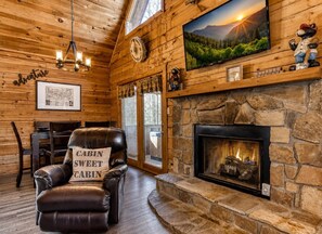 A cabin interior with a stone fireplace, leather armchair, wooden walls, and a mounted television. - Peaceful 2BR w/Hot Tub*Pool Table*Fireplace*Arcade (Sevierville)